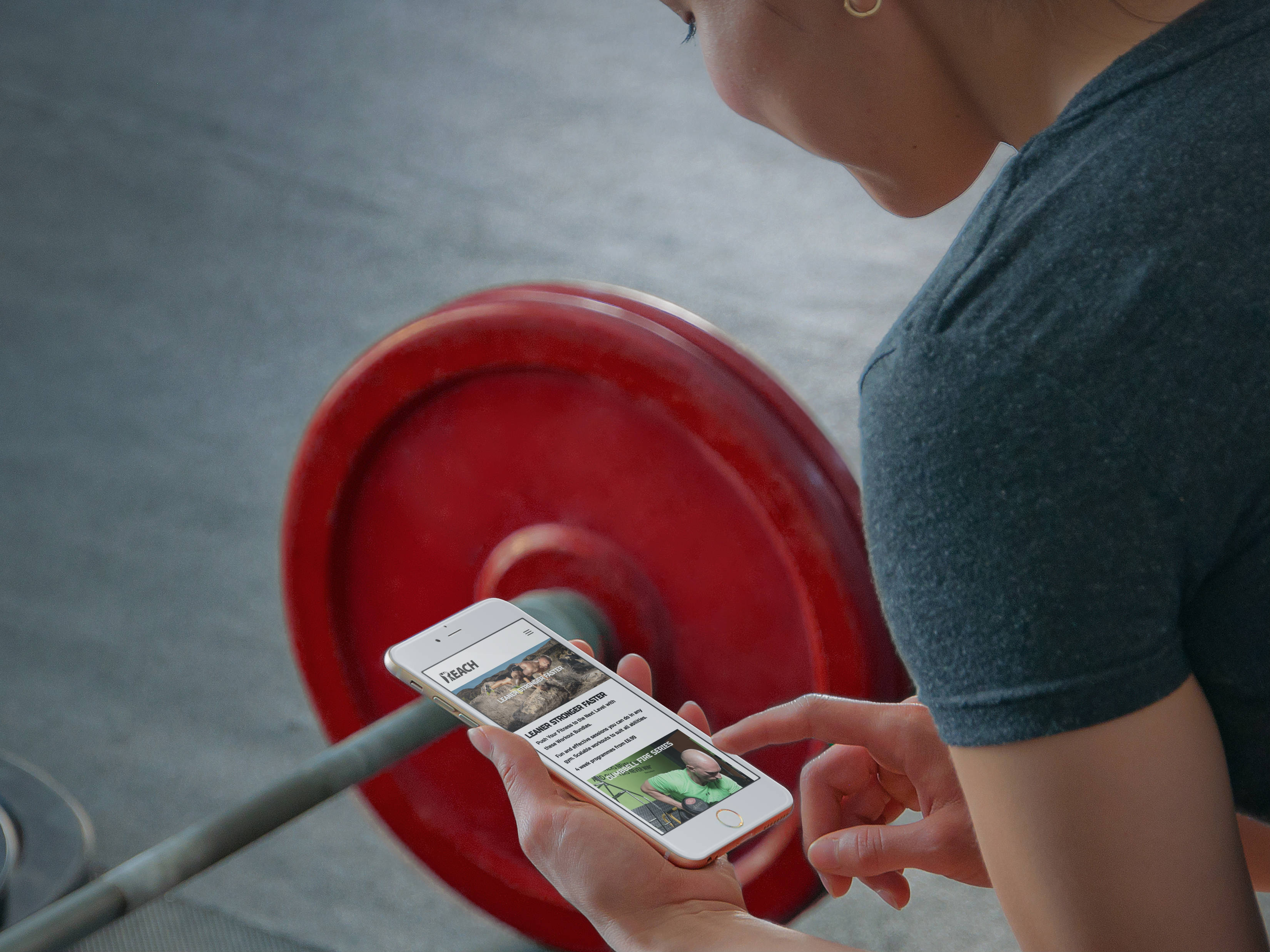 Reach Fitness user holds iPhone 6 rose gold with red bar bell